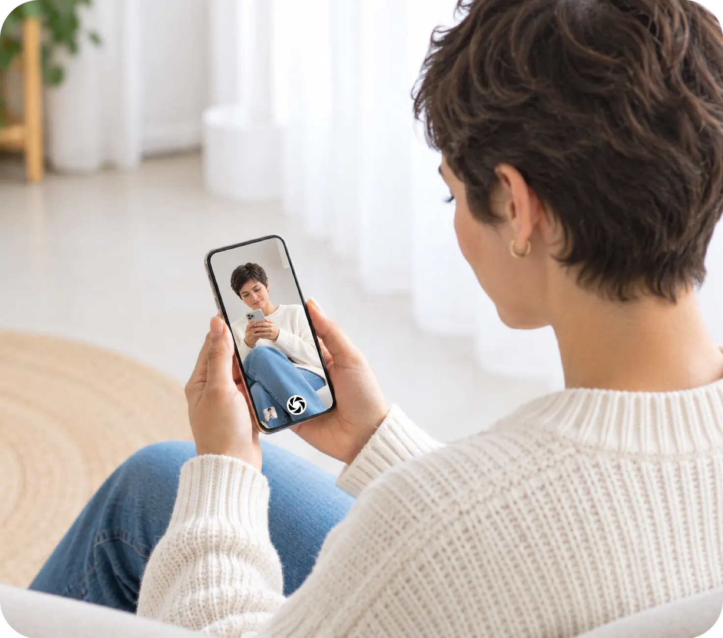 A woman on a sofa holds the See phone, which shows her own live picture from the Shoot phone across the room, with the shutter button at the bottom of the screen